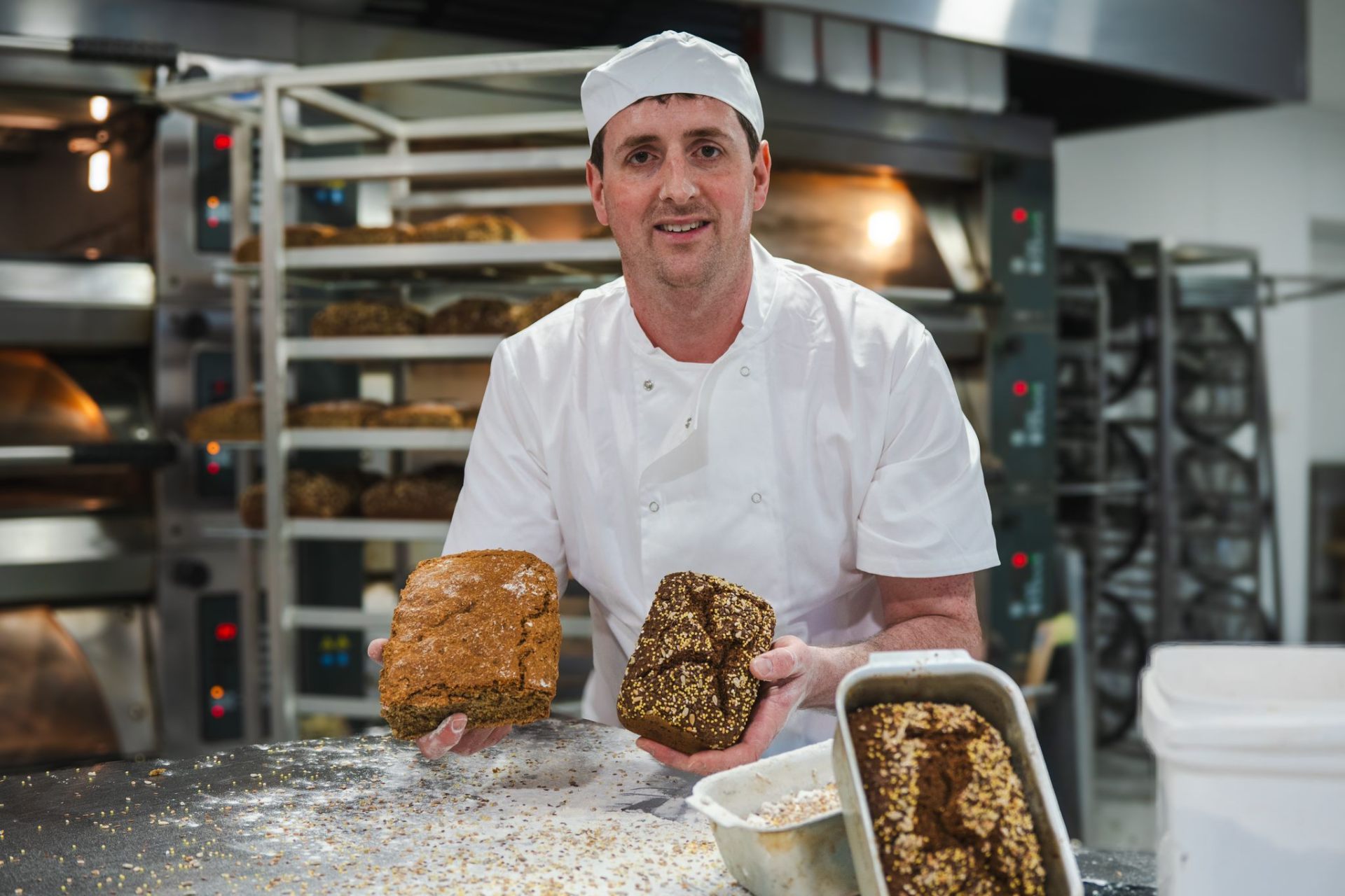 A baker at Philpott's holding a brown soda loaf and a seeded loaf, fresh from the oven